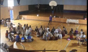 A group of children sitting on the floor in a gym.