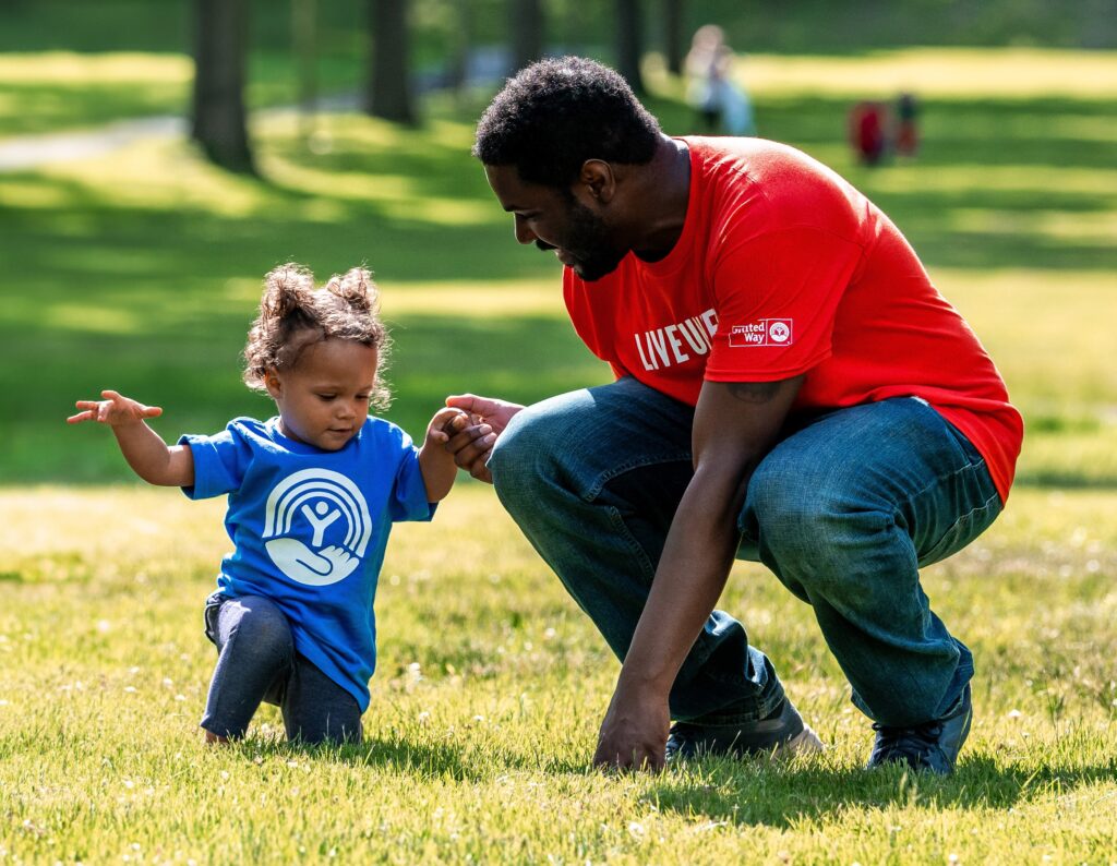 A father helping his daughter up while playing in the grass